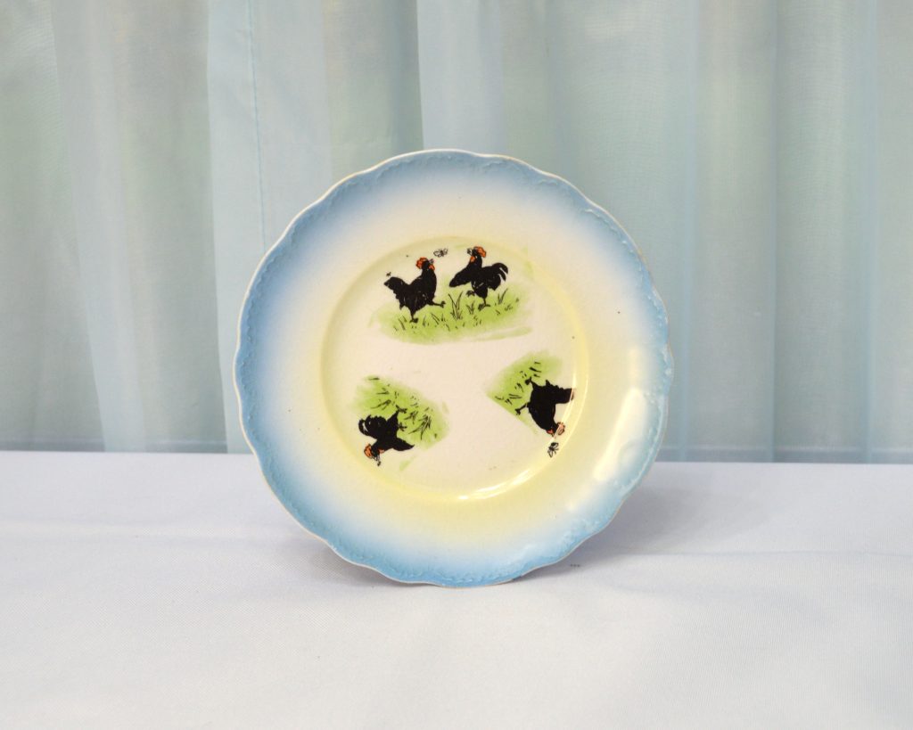 Small antique plate with blue border and decals of black roosters chasing moths.